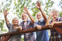 Bild: Vier Senioren, die von einem Balkon winken. 